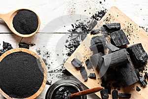 Black charcoal powder for facial mask and scrub, placed on a white wooden table, health and beauty concept