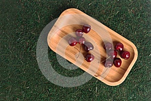 Black cherry on wooden plate isolated on green grass background flat lay