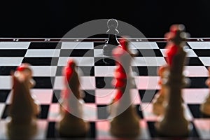 Black chess pawn against an army of white chess pieces on a chessboard on a black background