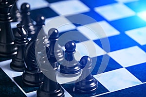 Black chess pieces on chess board with bright blue background light