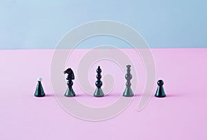 Black chess pieces standing in line on pink and blue background. Minimal arrangement