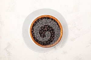 Black chickpeas in wooden bowl on light grey texured background, close-up. Selective focus, copy space