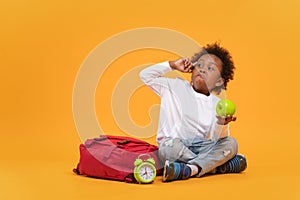 Black child boy 3 years, Student kid holding green apple in his hand and making a face sneer while sitting with red school bag and