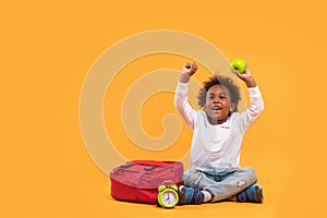 Black child boy 3 years, Student kid holding green apple in his hand and Yay! happy while sitting with school bag and alarm clock