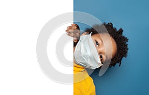 Black child boy in medical protective face mask holding white empty paper singbard