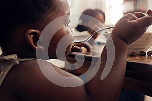 Black child, cereal spoon and eating baby in a home kitchen with food and bowl at breakfast. African girl, nutrition and