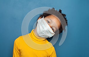 Black child in medical protective face mask on blue background