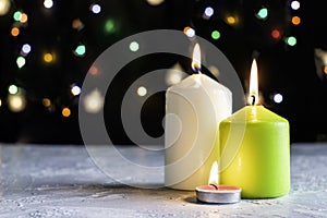 Black Christmas background with colorful lights and burning candles in the foreground