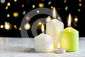 Black Christmas background with colorful lights and burning candles in the foreground