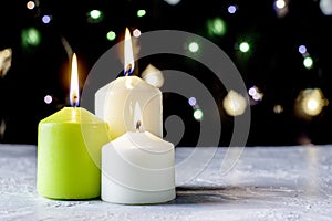 black Christmas background with colorful lights and burning candles in the foreground