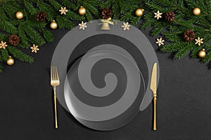 Black Christmas table setting with golden festive decor and fir branches. New Year serving with empty black plate. Copy space, top