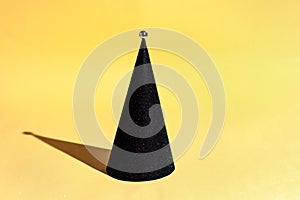 Black Christmas tree in the form of a cone on a yellow background in a minimalist style. Hi-tech christmas, new year