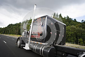 Black classic big rig semi truck with vertical pipes going on wi