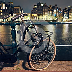 Black bike by the canal at night in Amsterdam