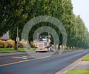 Black classic bonnet big rig semi truck with vertical pipes going on divided road with green trees