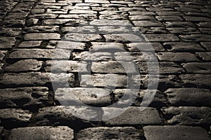 Black cobbled stone road background with reflection of light seen on the road. Black or dark grey stone pavement texture.