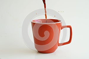Black coffee being poured into a red cup with a white background