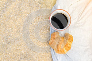 Black coffee and croissant on sand background, breakfast on the beach, food and drink concept