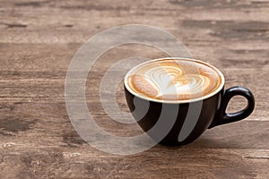 Black coffee cup of art latte with froth heart shaped  on wooden table. copy space for text design