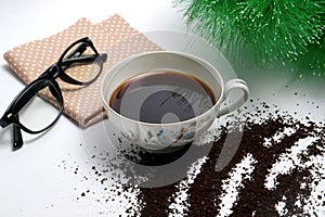 Black coffee in a cup with coarse coffee grounds and a brown cloth eyeglass on white background and green plant