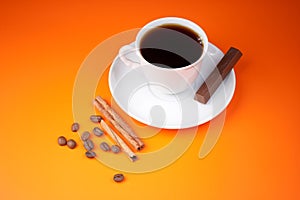 Black coffee cup on orange with piece of chocolate