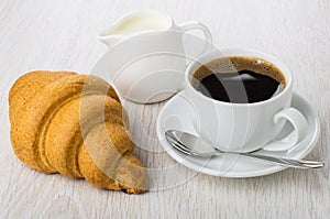 Black coffee in cup, spoon on saucer, croissant, milk