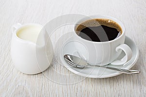Black coffee in cup, spoon on saucer, jug of milk