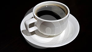 Black coffee drink. A white cup of black coffee on plate on dark table background. Morning coffee.