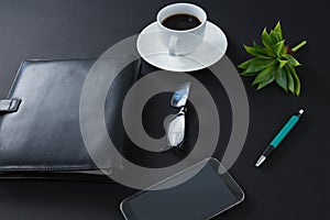 Black coffee, flora, pen, spectacles, mobile phone and organizer on black background