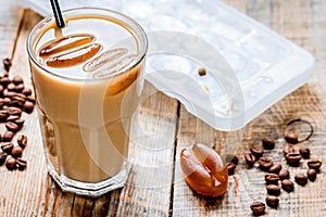 Coffee ice cubes and beans with latte on wooden desk background