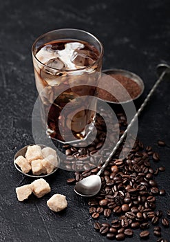 Black coffee with ice cubes and fresh milk with beans and cane sugar with ground coffee and long spoon on black