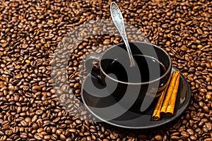 Black coffee mug and cinnamon sticks on the coffee beans background