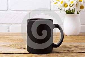 Black coffee mug mockup with chamomile bouquet in rustic vase