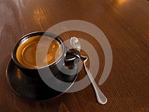 Black coffee mugs and spoon are placed on brown wood