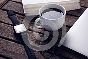 Black coffee with organizer, laptop, spectacles and smart watch on wooden table