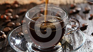 Black coffee is poured into glass transparent cup on saucer