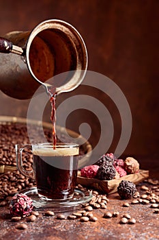 Black coffee is poured into a small glass cup from a copper coffee maker