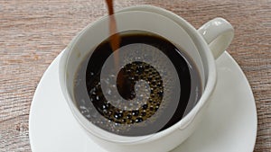 Black coffee pouring from jar to cup on table