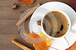 Black coffee with a saucer, orange autumn maple leaves, cinnamon sticks, anise stars on a brown wooden