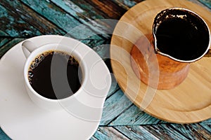 Black coffee served in a white cup. Copper cezve on bamboo stand. Traditional turkish method