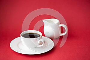 black coffee in small white coffee cup and milk jug on red background