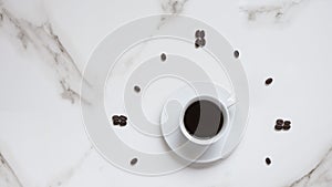 Black coffee in white ceramic cup and coffee beans pattern in clock face forming on white marble tabletop