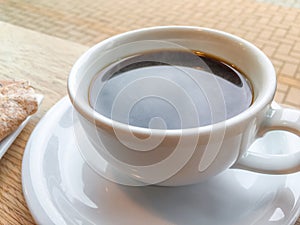 Black coffee in white ceramic cup and saucer in a cafe under even natural light.