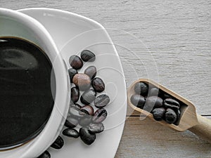 Black coffee in a white ceramic mug and coffee beans in a dish on a wooden floor