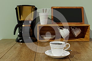 Black coffee in a white ceramic mug with gold rim and saucer. Blur Black and gold espresso machine  and Coffee cup storage on