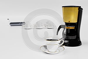 Black coffee in a white ceramic mug with gold rim and saucer. Black and gold espresso machine on white background and white