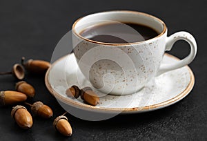 Black coffee in a white cup and acorns. Acorn coffee on a black background. The concept of a caffeine substitute