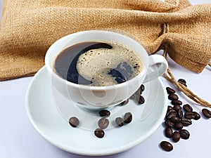 Black coffee in white cup, coffee beans on old wooden texture background.