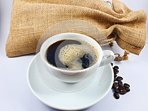 Black coffee in white cup, coffee beans on old wooden texture background.