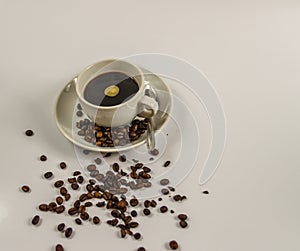 Black coffee in a white cup on saucer with spoon and spilled coffee beans